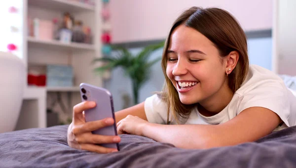 Sorrindo Adolescente Menina Deitada Cama Casa Olhando Para Telefone Móvel — Fotografia de Stock