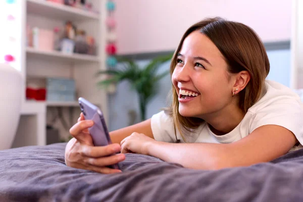 Sorrindo Adolescente Menina Deitada Cama Casa Olhando Para Telefone Móvel — Fotografia de Stock