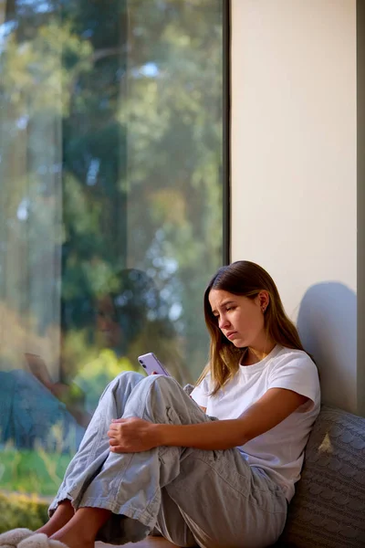 Θλιβερό Έφηβο Κορίτσι Κάθεται Στο Παράθυρο Στο Σπίτι Κοιτάζοντας Κινητό — Φωτογραφία Αρχείου