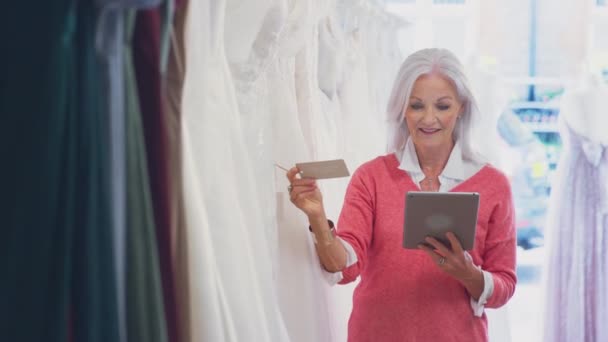 Inhaberin Eines Brautgeschäfts Blickt Durch Hochzeitskleider Mit Digitalem Tablet Aufgenommen — Stockvideo