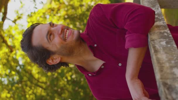 垂直ビデオポートレートのカジュアルな服を着て笑顔成熟した男は夏の田舎を歩く上で木製のフェンスにもたれて スローモーションで撮影 — ストック動画