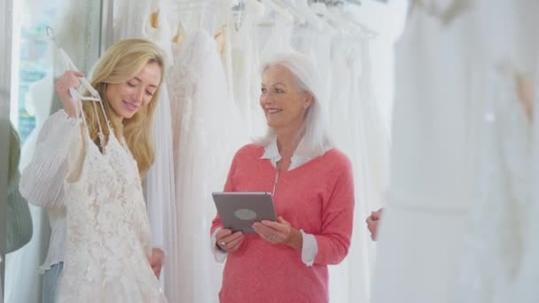 售货员或拥有数码平板电脑的店主帮助在婚纱商店里带着成年女儿的母亲选择婚纱 慢镜头拍摄 — 图库视频影像