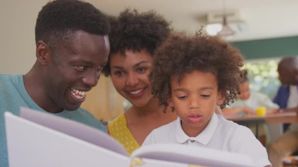 両親がソファの上に座っているマルチ世代の家族家庭読書本で息子と祖父母が孫の宿題を背景に助けています スローモーションで撮影 — ストック動画