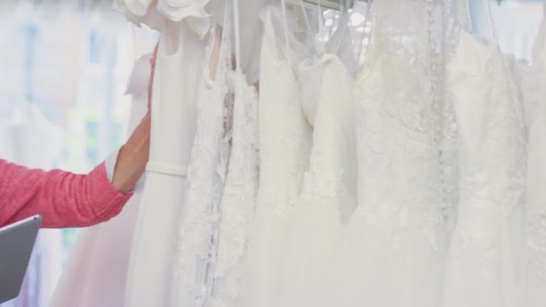 Inhaberin Eines Brautgeschäfts Blickt Durch Hochzeitskleider Mit Digitalem Tablet Aufgenommen — Stockvideo