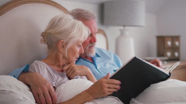 Glimlachend Gepensioneerd Senior Paar Bed Thuis Kijkend Door Fotoalbum Oude — Stockvideo