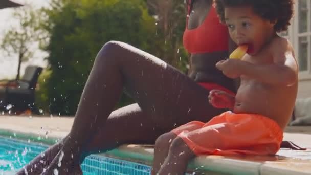 가족의 여름휴가 수영장 가장자리에 얼음과자를 먹으면서 어머니와아 물장구를 동작으로 — 비디오
