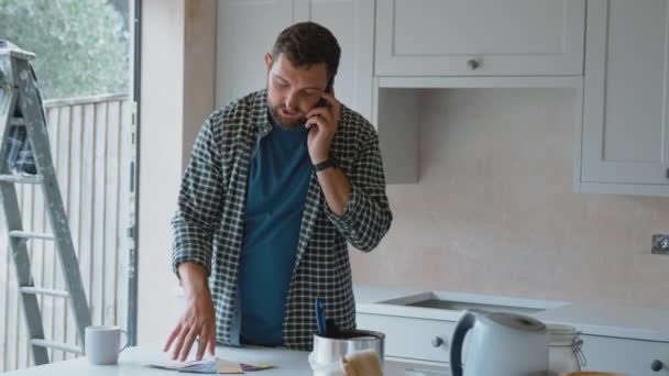 男性改装キッチン自宅で塗料の色の腕時計を見て 携帯電話で話して スローモーションで撮影 — ストック動画