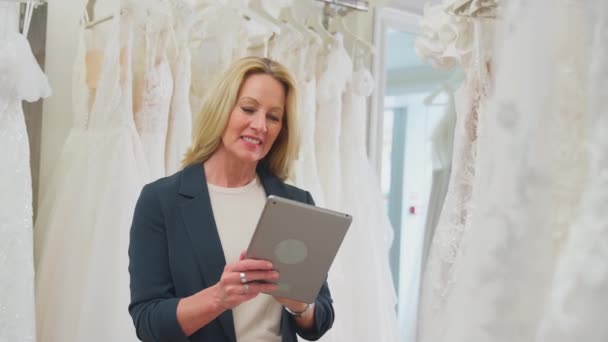 Dojrzała Właścicielka Sklepu Ślubnego Patrząca Przez Suknie Ślubne Cyfrową Tabletką — Wideo stockowe