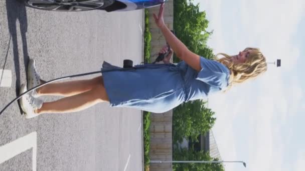 電気自動車に充電ケーブルを取り付ける屋外の女性の垂直ビデオ スローモーションで撮影 — ストック動画