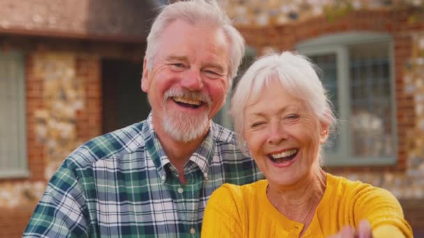 Uśmiechnięta Para Seniorów Opierająca Się Bramie Przed Wymarzonym Domkiem Trzymająca — Wideo stockowe