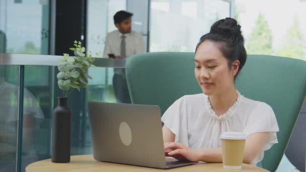 オフィスビルのブレイクアウトシーティングエリアでテーブルで働くラップトップを使用し テイクアウトコーヒーを飲むビジネスマン スローモーションで撮影 — ストック動画