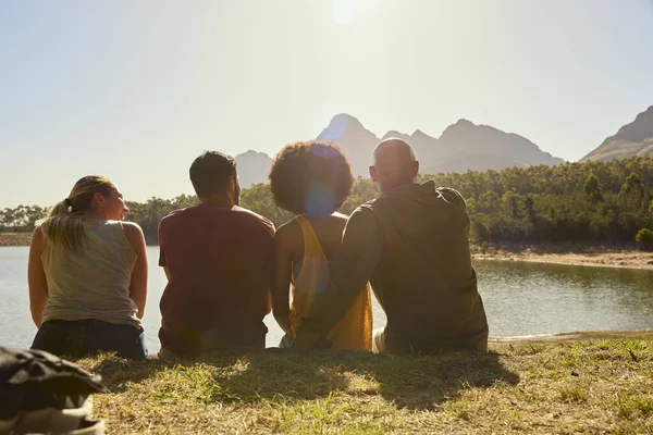 Bakifrån Grupp Vänner Med Ryggsäckar Semester Vandring Sitter Vid Sjön — Stockfoto