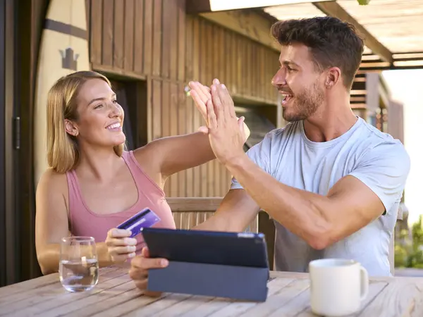 Couple With Credit Card Using Digital Tablet At Home To Book Holiday Or Shop Online Giving High Five