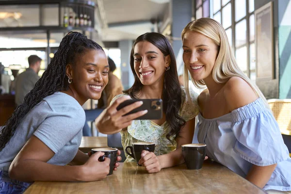 Group Of Female Friends Meeting Up In Restaurant Or Coffee Shop Posing For Selfie On Mobile Phone
