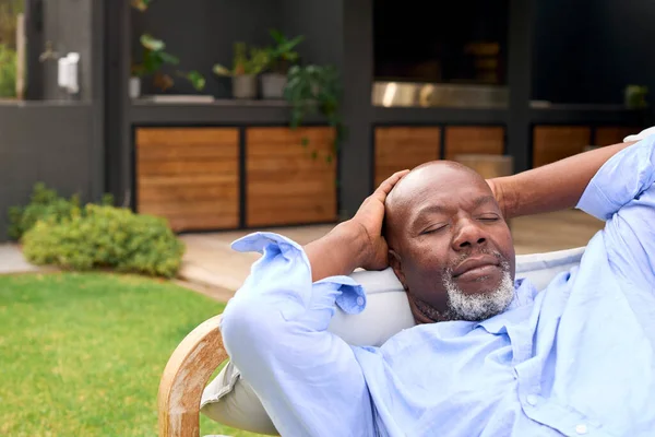 Senior Man Sleeping On Outdoor Seat In Garden At Home