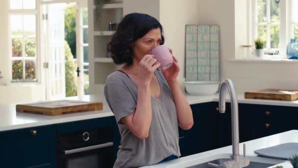笑着站在厨房柜台边的独立而成熟的女人 一边喝着热饮一边休息 慢镜头拍摄 — 图库视频影像