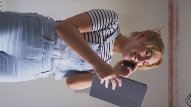 デジタルタブレットの女性の垂直ビデオは 家で部屋を改装し 壁にテスターペイントカラーストリップを見ているデジタルタブレットを保持するオンラインインスピレーションを得る スローモーションで撮影 — ストック動画