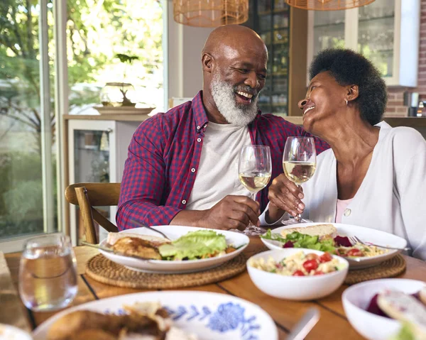 Loving Senior Couple Sitting Around Table At Home Enjoying Meal With Wine Together