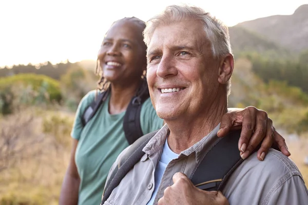 Senior Couple With Backpacks Hiking In Countryside Together