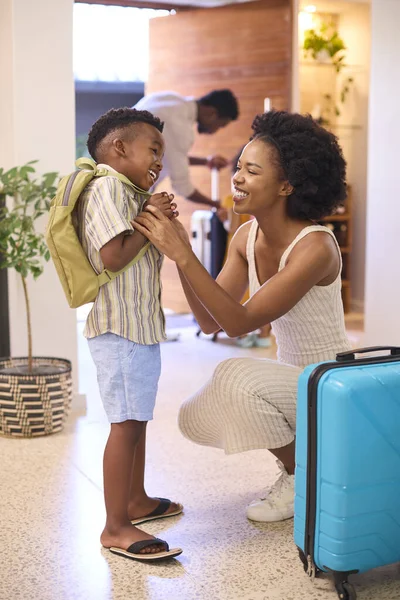 Mother Helping Son Get Ready With Backpack As Family Leave Home For Holiday Or Vacation