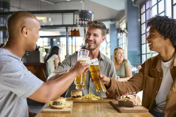 stock image Group Of Male Friends Meeting Up In Bar Eating Burgers And Doing Cheers With Beer