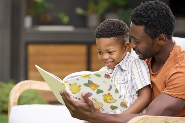 Family Shot With Smiling Father And Son Reading Book In Garden Together