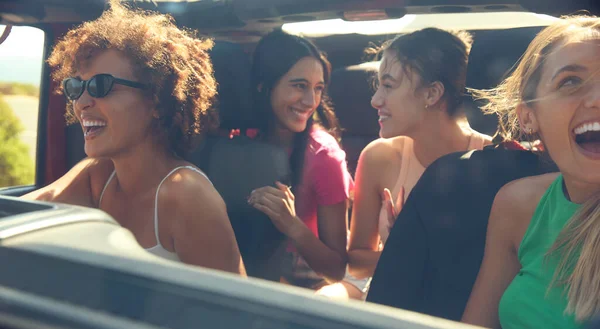 View Through Windscreen Of Group Of Laughing Female Friends Having Fun In Open Top Car On Road Trip