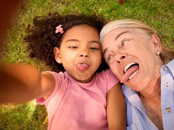 携帯電話でセルフィーを取る草の上に横たわっている祖母と孫娘のPovオーバーヘッドショット — ストック写真