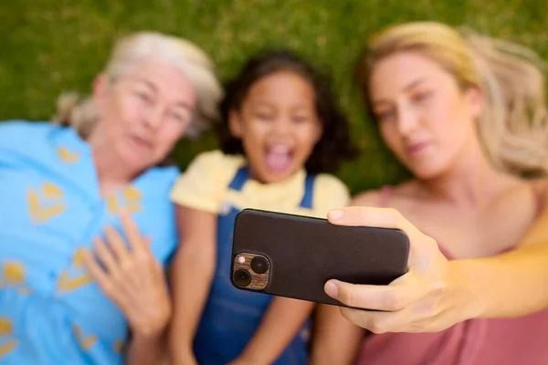 多代女性家庭躺在草地上用手机自拍的间接镜头 — 图库照片