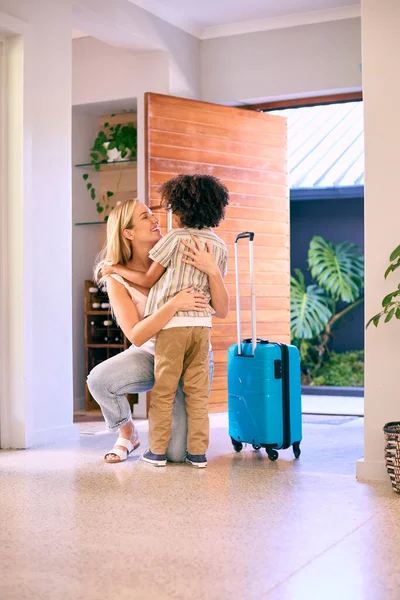 Son Greeting Mother Returning Home With Luggage From Trip Away
