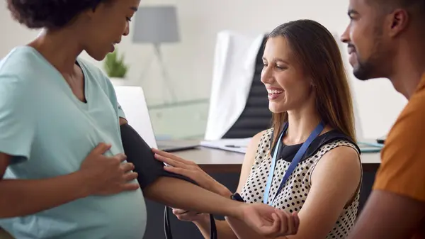 与女医生或全科医生预约的怀孕夫妇在任期间测量血压 免版税图库照片