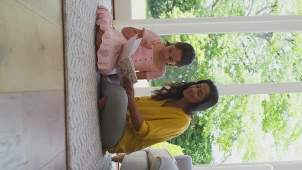 自宅の読書本でラウンジに座っている母と娘の垂直ビデオ スローモーションで撮影 — ストック動画