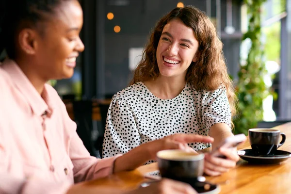 stock image Two Young Female Friends Meeting In Coffee Shop And Looking At Mobile Phone Together