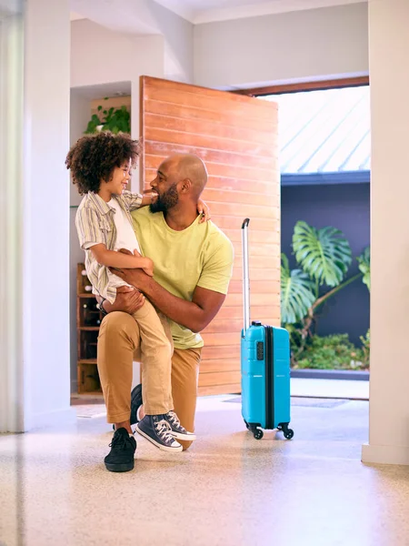 Son Greeting Father Returning Home With Luggage From Trip Away
