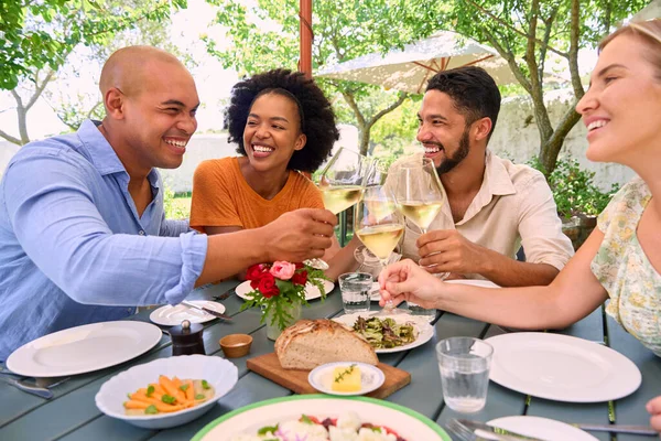 Group Of Friends Enjoying Outdoor Meal And Wine On Visit To Vineyard Restaurant With Cheers