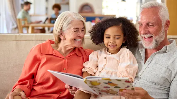 Enkelin Liest Mit Großeltern Auf Sofa Hause Mit Eltern Hintergrund — Stockfoto