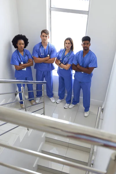 Portrait Of Multi Cultural Medical Team Wearing Scrubs Standing On Stairs In Hospital