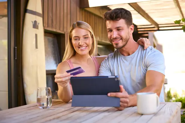 Excited Couple With Credit Card Using Digital Tablet At Home To Book Holiday Or Shop Online