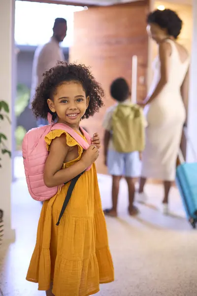 Portrait Of Girl By Door With Backpack As Family Leave Home For Holiday Or Vacation