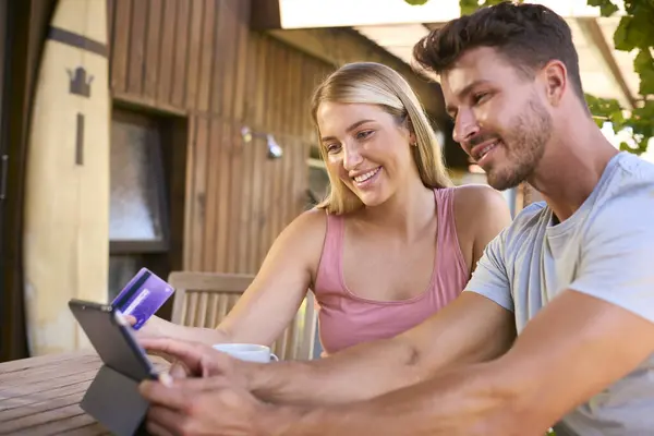 Excited Couple With Credit Card Using Digital Tablet At Home To Book Holiday Or Shop Online