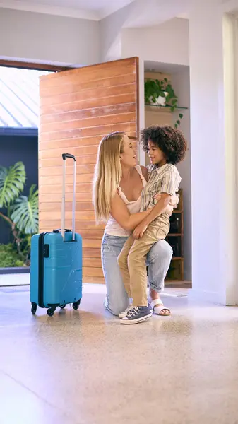Son Greeting Mother Returning Home With Luggage From Trip Away