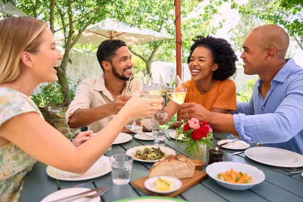 Group Of Friends Enjoying Outdoor Meal And Wine On Visit To Vineyard Restaurant With Cheers