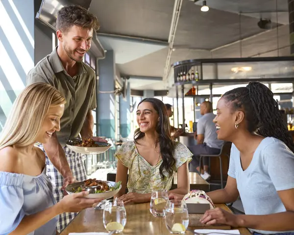 Group Of Female Friends Meeting Up In Restaurant Being Served Meal By Waiter