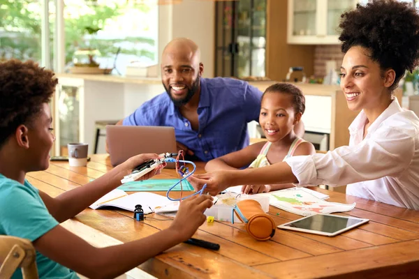 家庭围坐在家里用笔记本电脑和父母一起帮助孩子做科学作业 — 图库照片