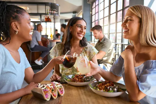 Group Of Female Friends Meeting Up In Restaurant Eating Food And Doing Cheers With Meal