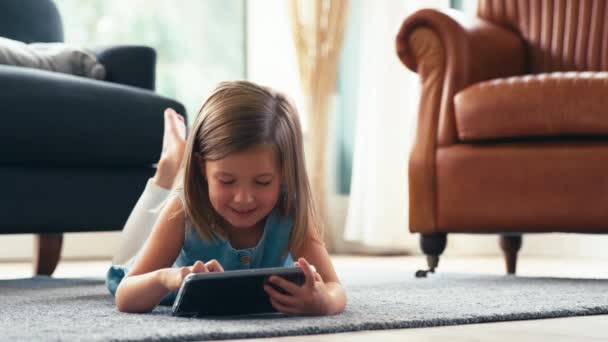 自宅でラウンジの床に横たわる若い女の子は ゲームをプレイしたり デジタルタブレットに映画をストリーミングしたり スローモーションで撮影 — ストック動画