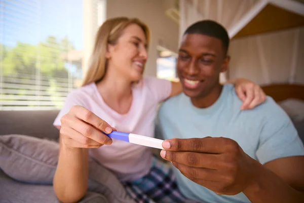 Excited Multi-Racial Couple In Bedroom At Home Celebrating Positive Pregnancy Test Result
