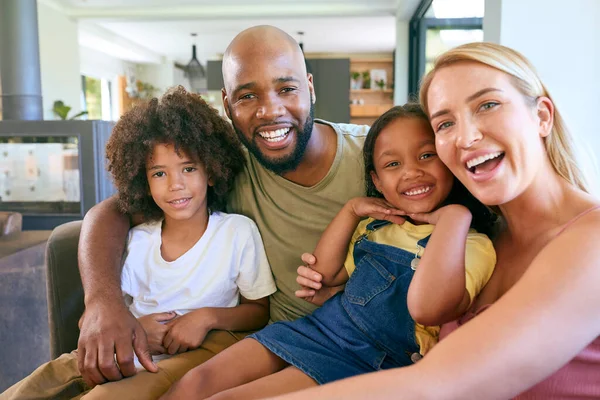 Portrait Of Smiling Family Hugging And Sitting On Sofa At Home Together