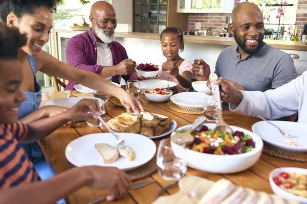 一緒に食事のための食糧を提供するテーブルの周りに座る多世代の家族 — ストック写真