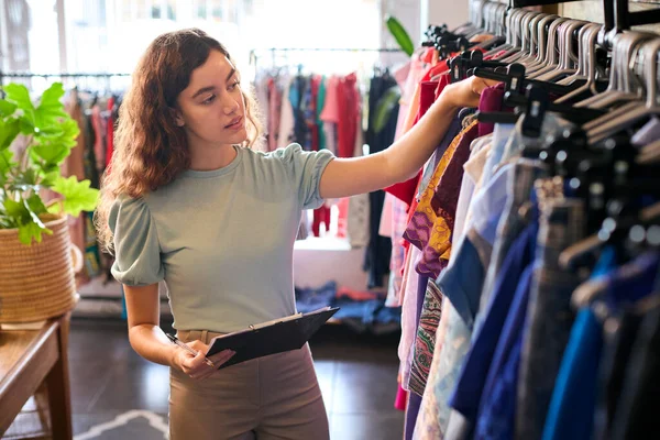 Female Owner Or Worker In Fashion Clothing Store Checking Stock With Clipboard